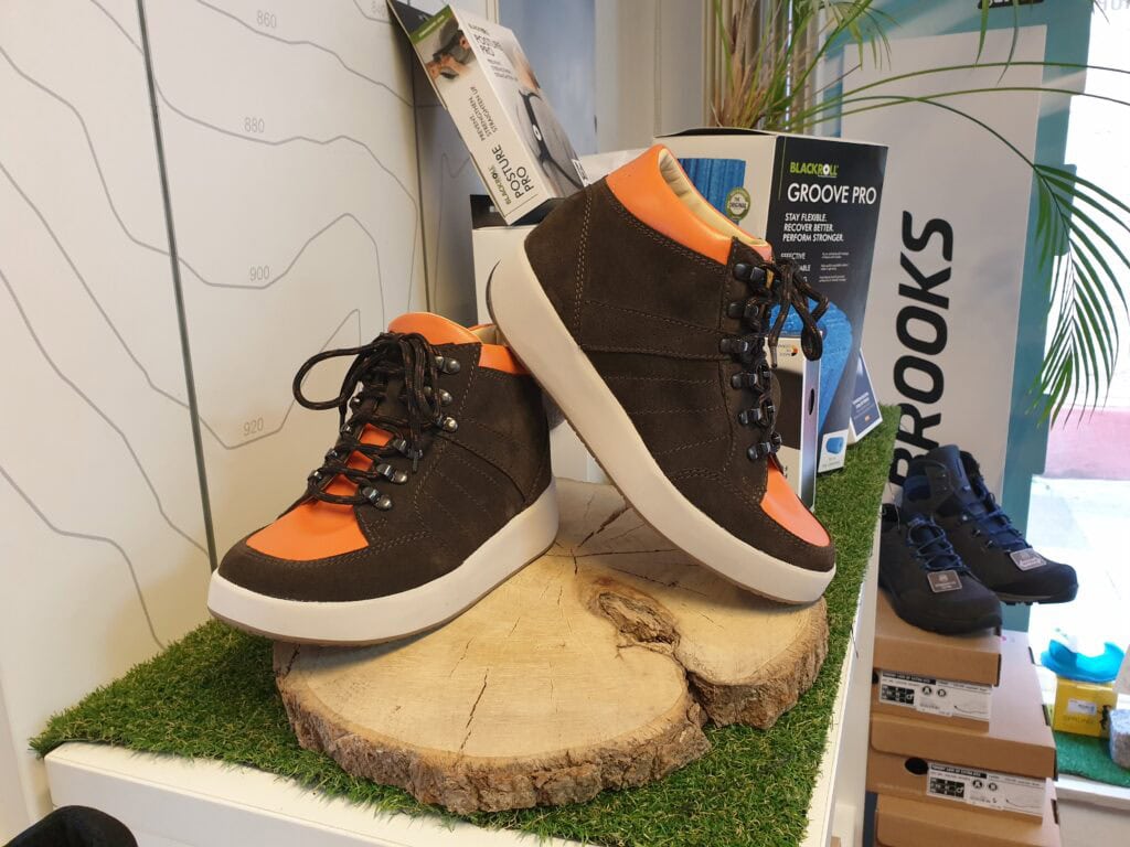 Schuhschnittvital, Vitalschuh in Schwarz-Orange auf Holzscheibe, orthopädischer Gesundheitsschuh, komfortabler Sportschuh, moderne Fußpflege, ergonomisches Design, orthopädische Schuhe, Gesundheitsschuhe, ergonomisches Schuhwerk, Schuheinlage, Fußgesundheit.