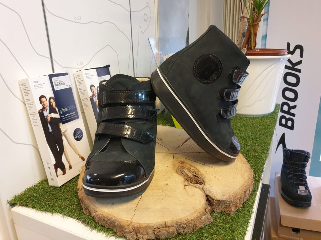 Latschen und orthopädische Schuhmodelle von SCHRITT VITAL auf einem Holzstück mit Grasteppich, ideal für gesunde Füße und Fußgesundheit.